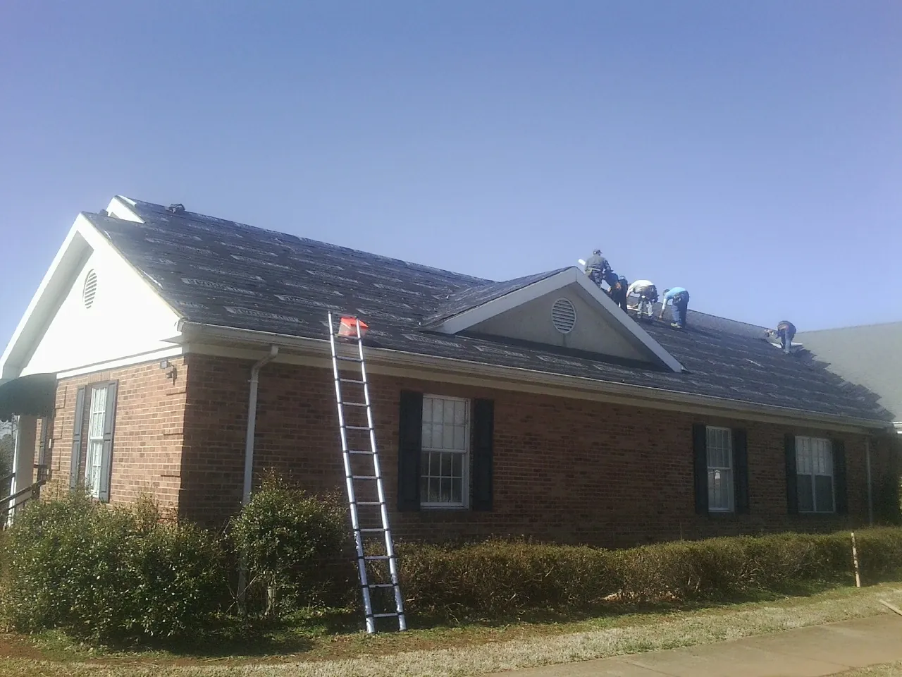 Crew tearing shingles off a brick ranch roof with a ladder set — Metal Roof Repair work by our crew in Edgewater