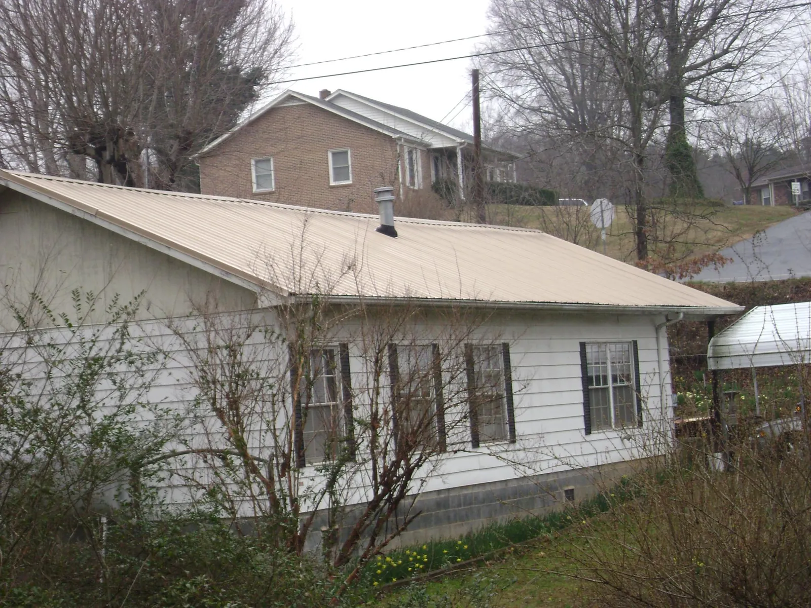 Tan metal roof on a white sided house set into a hillside — Commercial Roofing by Roofing Brothers in Edgewater